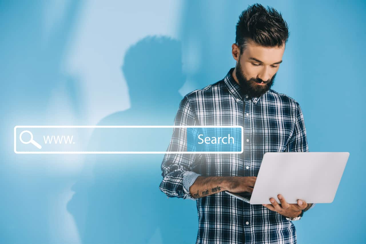 Man Standing With Laptop In Hand Typing With Search Bar Superimposed