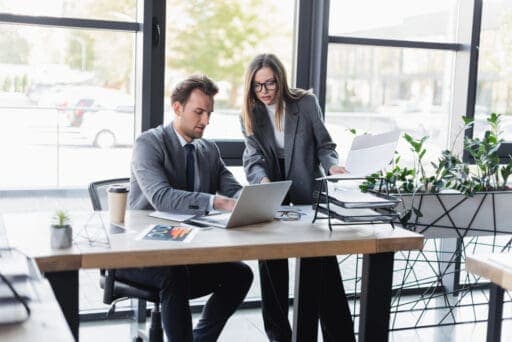 Landscape photo example: two coworkers reviewing papers at a laptop in a bright office